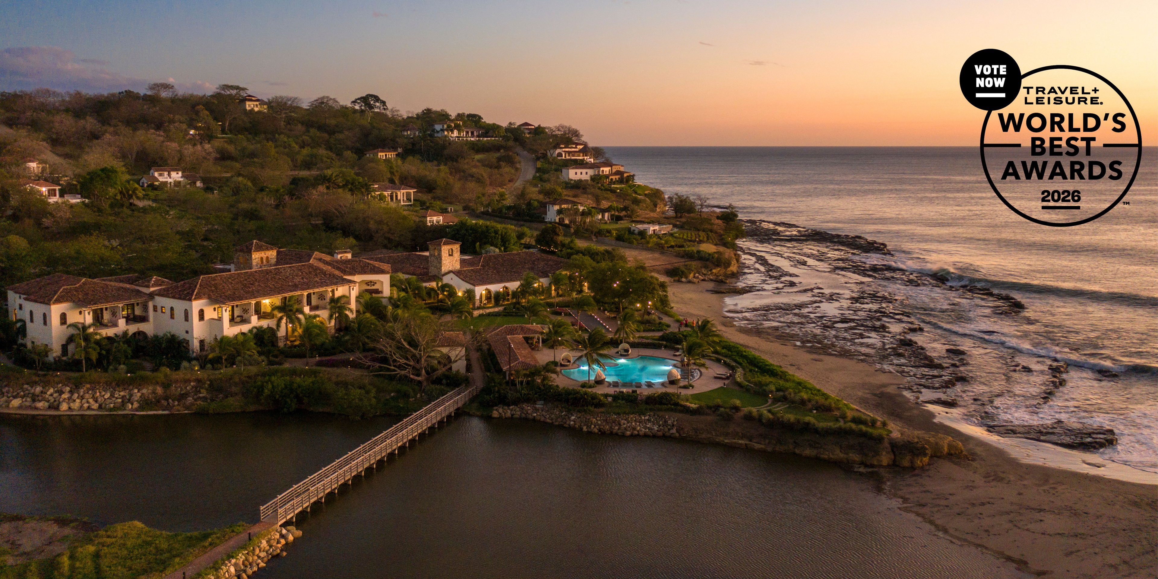 Golden hour bathes the colonial-style resort in warm light, where an infinity pool meets pristine coastline and a wooden pier extends into tranquil waters.