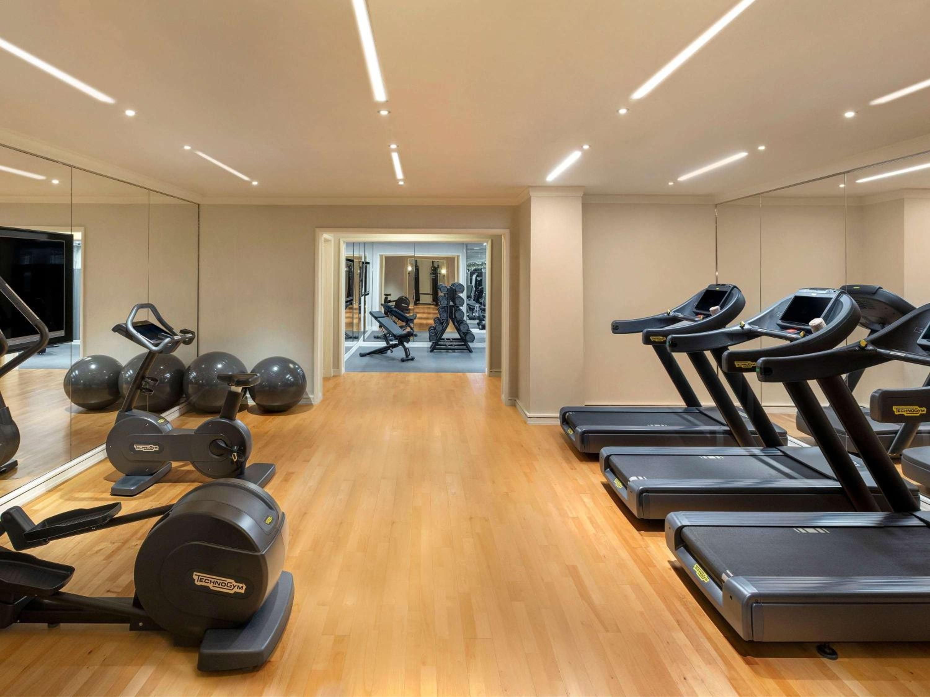 Sleek TechnoGym equipment lines polished wood floors beneath modern linear lighting, creating an upscale fitness sanctuary that rivals Manhattan's premium gyms.