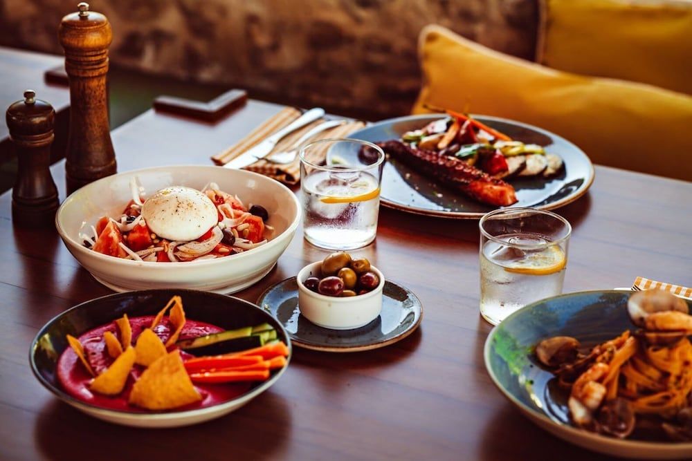 Mediterranean mezze spreads across weathered wood tables as golden hour light catches crystal glasses filled with citrus-spiked gin, creating an intimate tapas ritual.