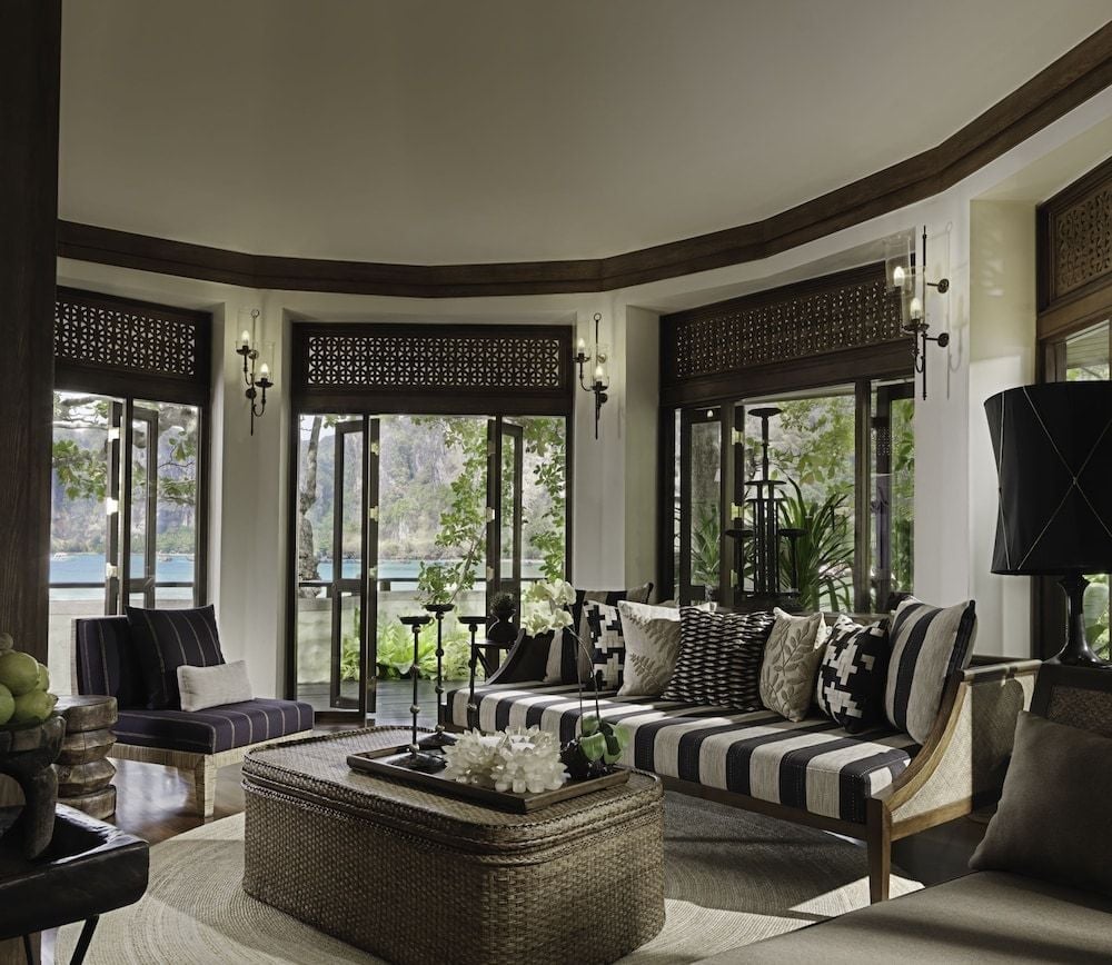 Curved windows frame limestone karsts beyond while striped cushions and woven textures create an intimate seating nook where tropical breezes meet refined comfort.