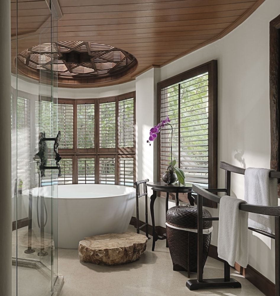 Carved stone basins and weathered wood textures create a spa-like sanctuary where tropical breezes filter through louvered windows, bringing jungle whispers indoors.