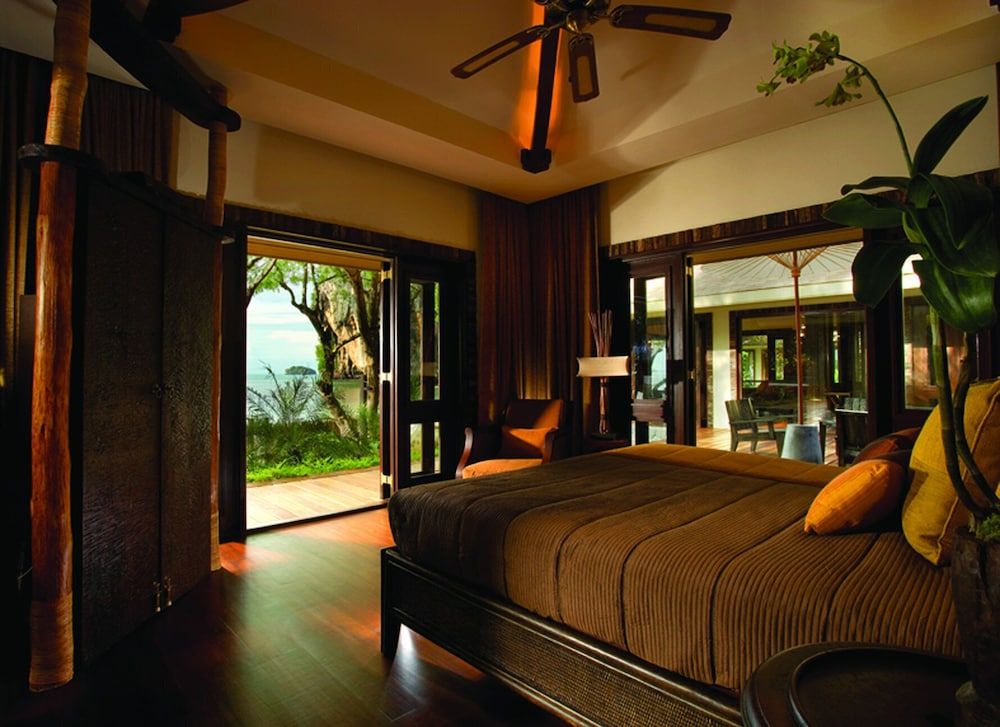 Warm teak floors and rich earth tones create an intimate sanctuary where tropical breezes drift through open doors, revealing lush jungle canopy beyond.