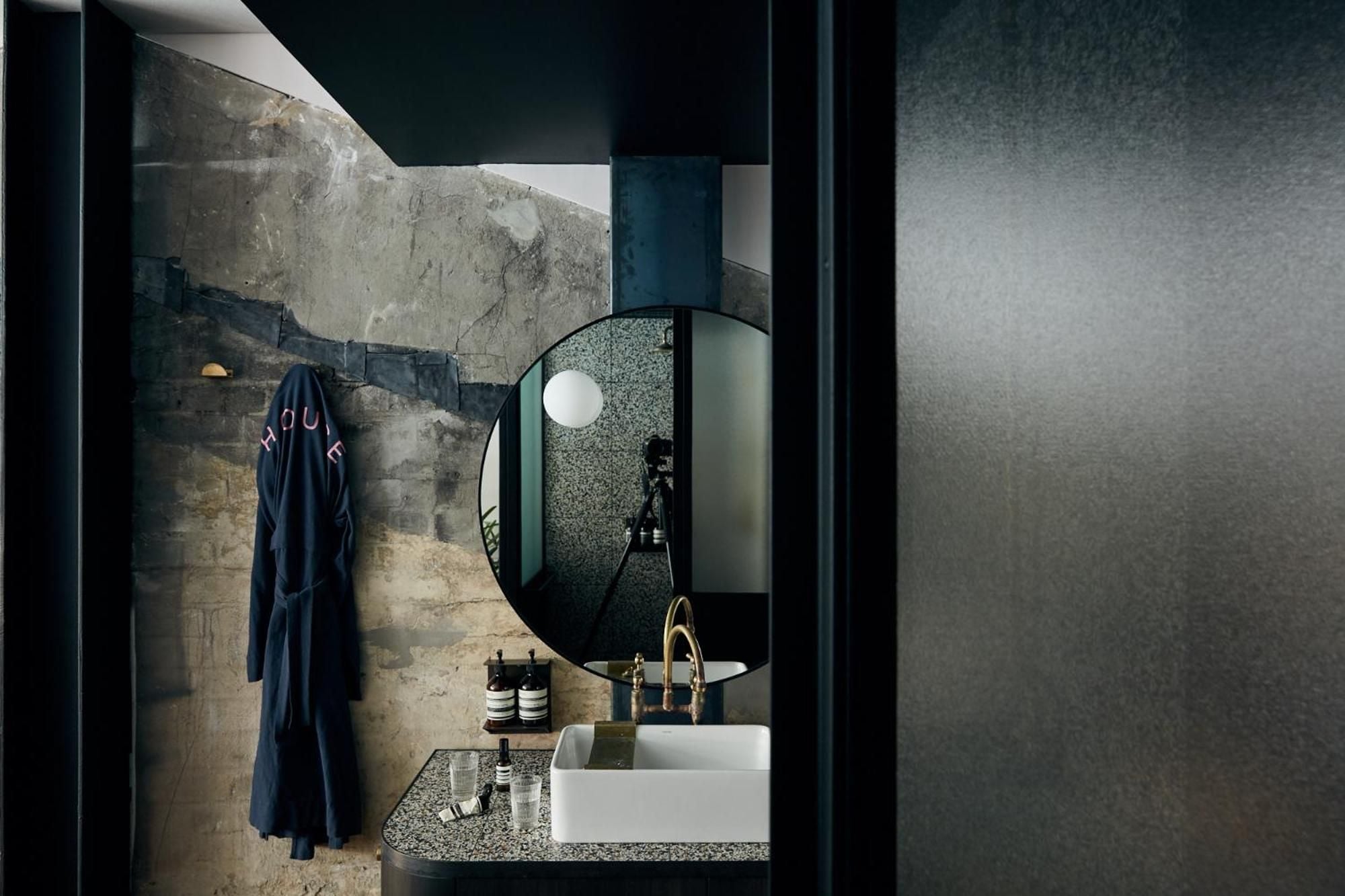 Raw concrete meets polished sophistication in this moody powder room, where speckled terrazzo surfaces and brass fixtures create an unexpectedly luxurious industrial sanctuary.