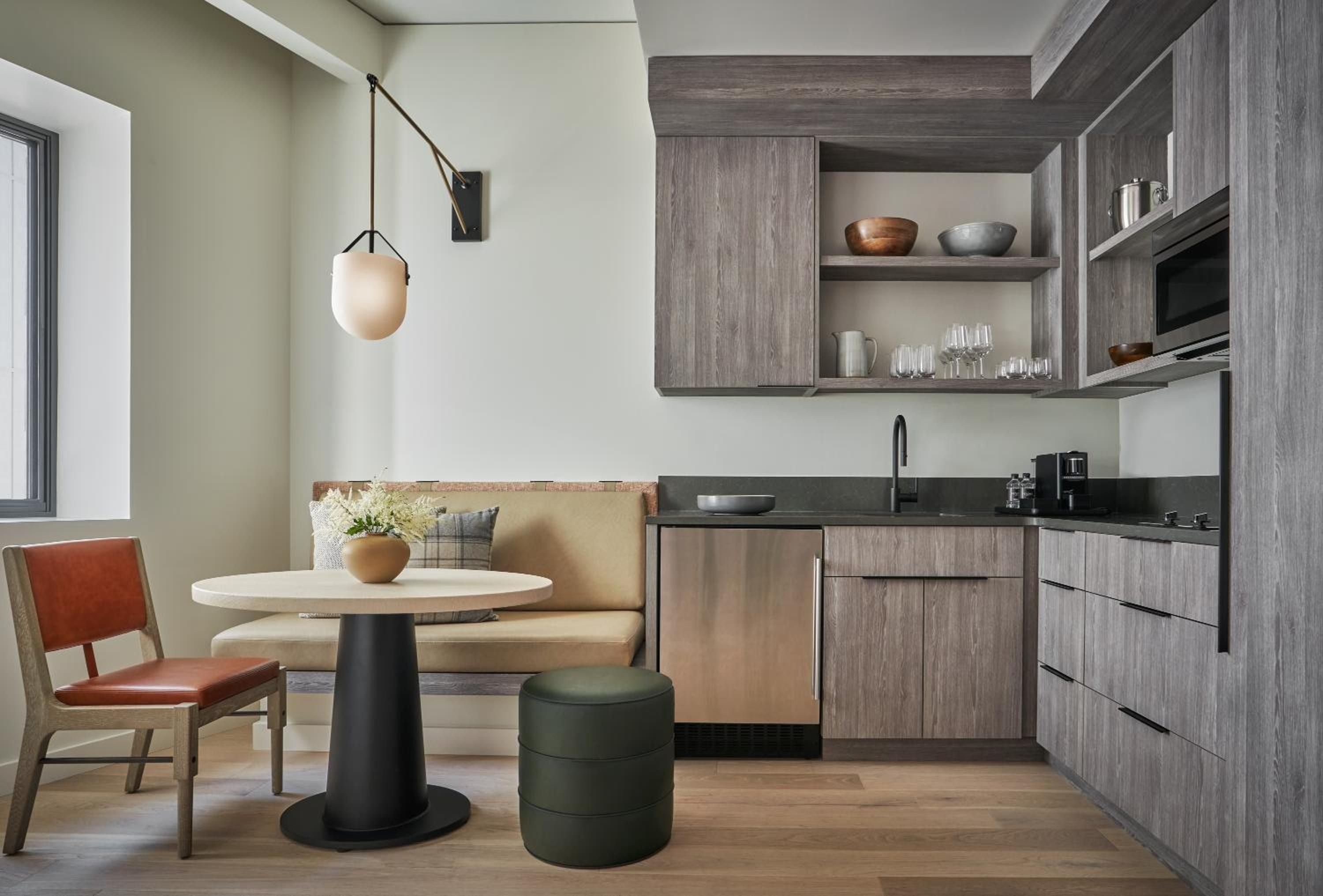 Warm wood cabinetry and sage-green accents create an intimate kitchenette where copper bowls catch morning light streaming through oversized windows.