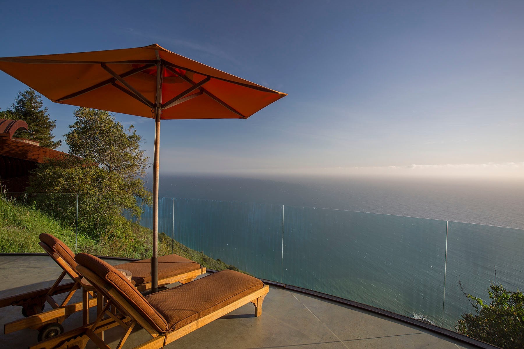 Teak loungers and burnt orange umbrellas frame the endless Pacific horizon from clifftop terraces where Big Sur's dramatic coastline unfolds below.