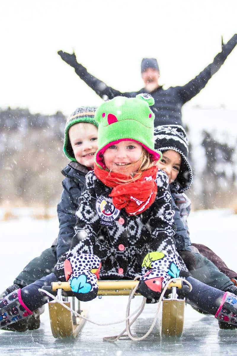 Families bundle up for exhilarating sled rides across snow-dusted meadows, their laughter echoing through the crisp Montana air as snowflakes dance around rosy cheeks.