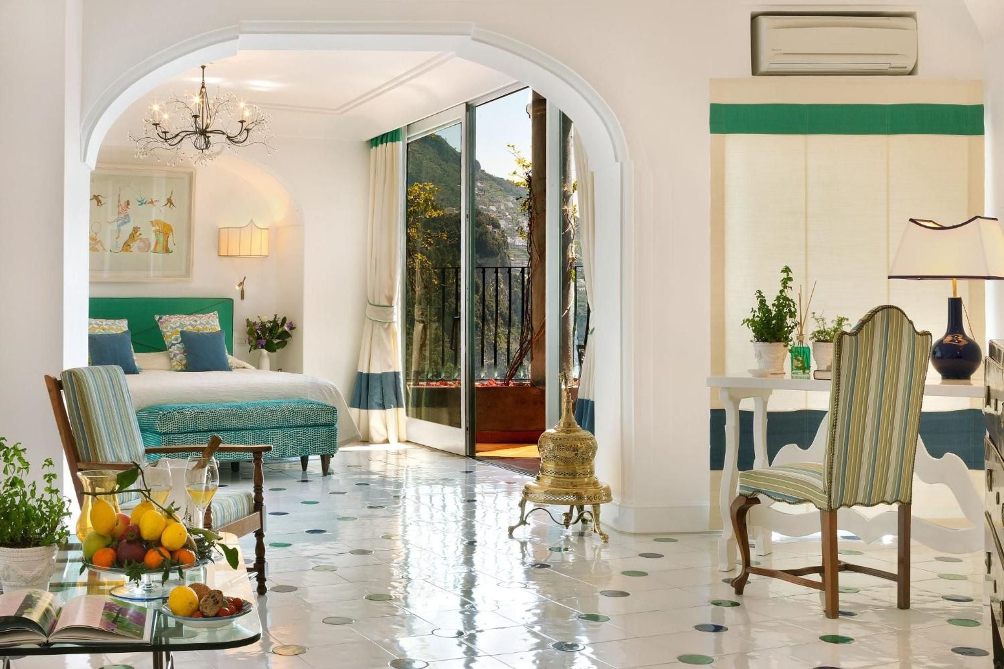 Polished marble floors adorned with colorful ceramic dots lead through graceful archways to a emerald-accented suite overlooking Positano's dramatic coastline.