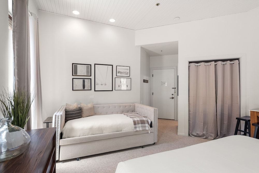 Soft gray tones and plush daybed create a serene retreat, where filtered light plays across neutral linens and carefully curated artwork adorns pristine white walls.