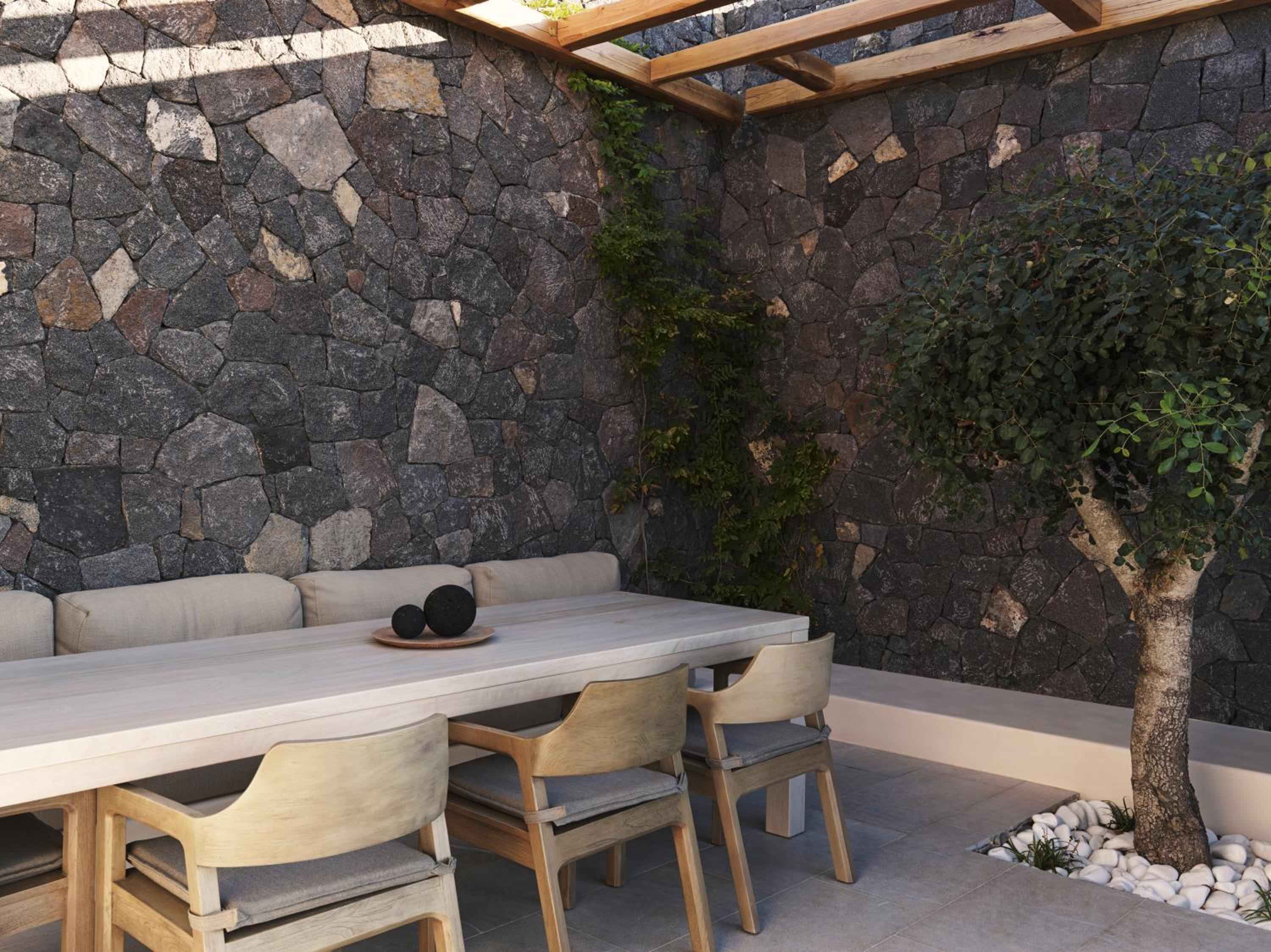 Natural stone walls frame an intimate dining corner where weathered wood meets volcanic rock, creating Santorini's most sophisticated al fresco experience.