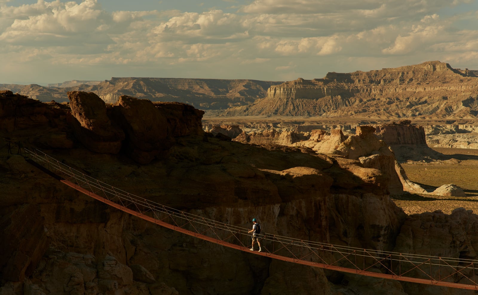 A suspension bridge spans dramatic canyon walls, offering guests an adventurous pathway through Amangiri's breathtaking Utah desert landscape at golden hour.