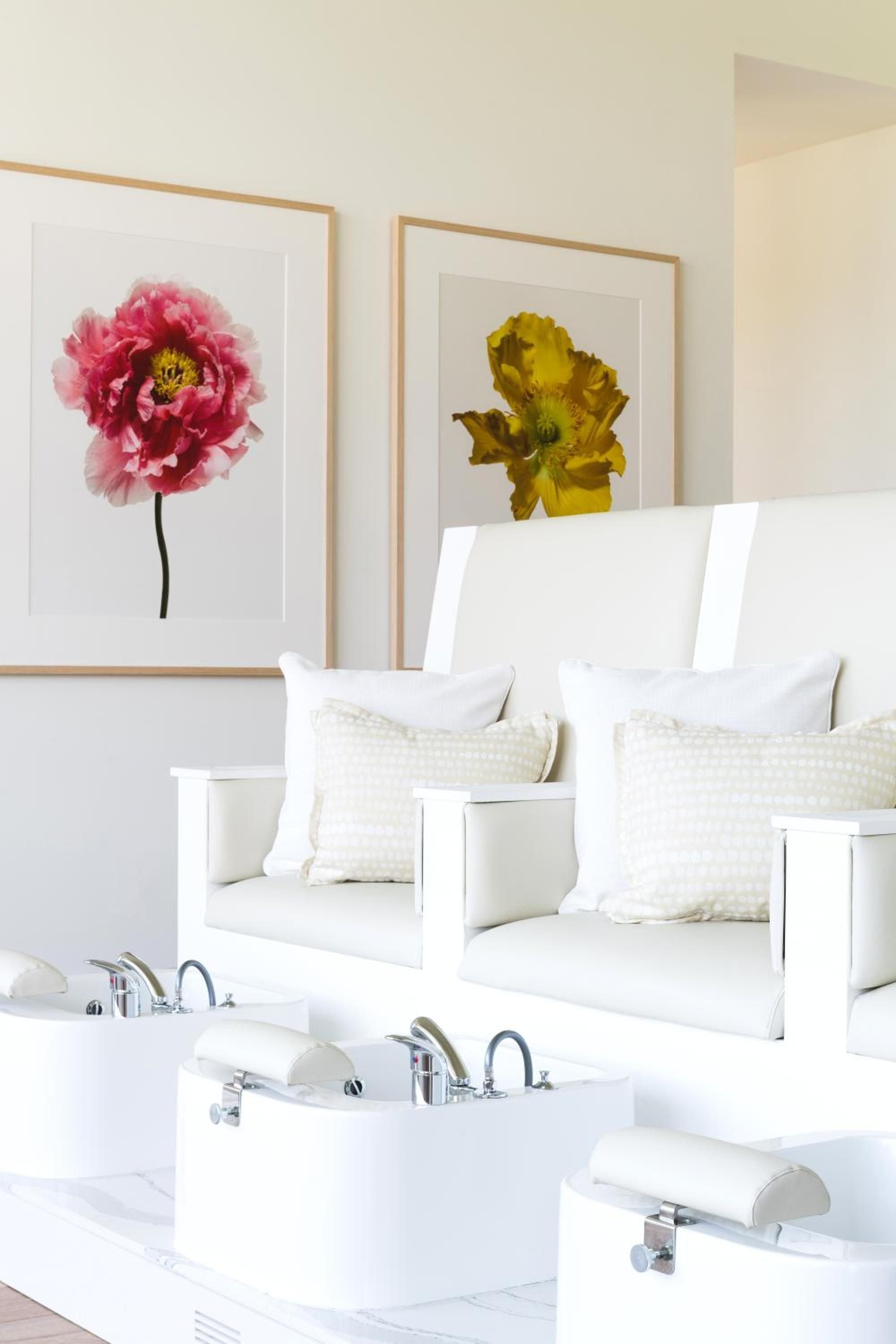 Sunlight streams across pristine white marble soaking tubs while vibrant botanical prints add pops of color to this serene couples' spa retreat.