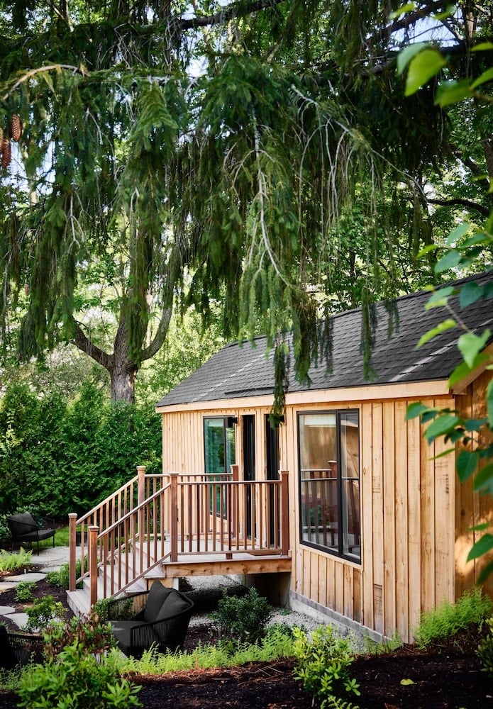 Cedar-shingled cabin nestled beneath graceful weeping willow branches, where natural wood railings and thoughtful landscaping create an intimate forest retreat feeling.