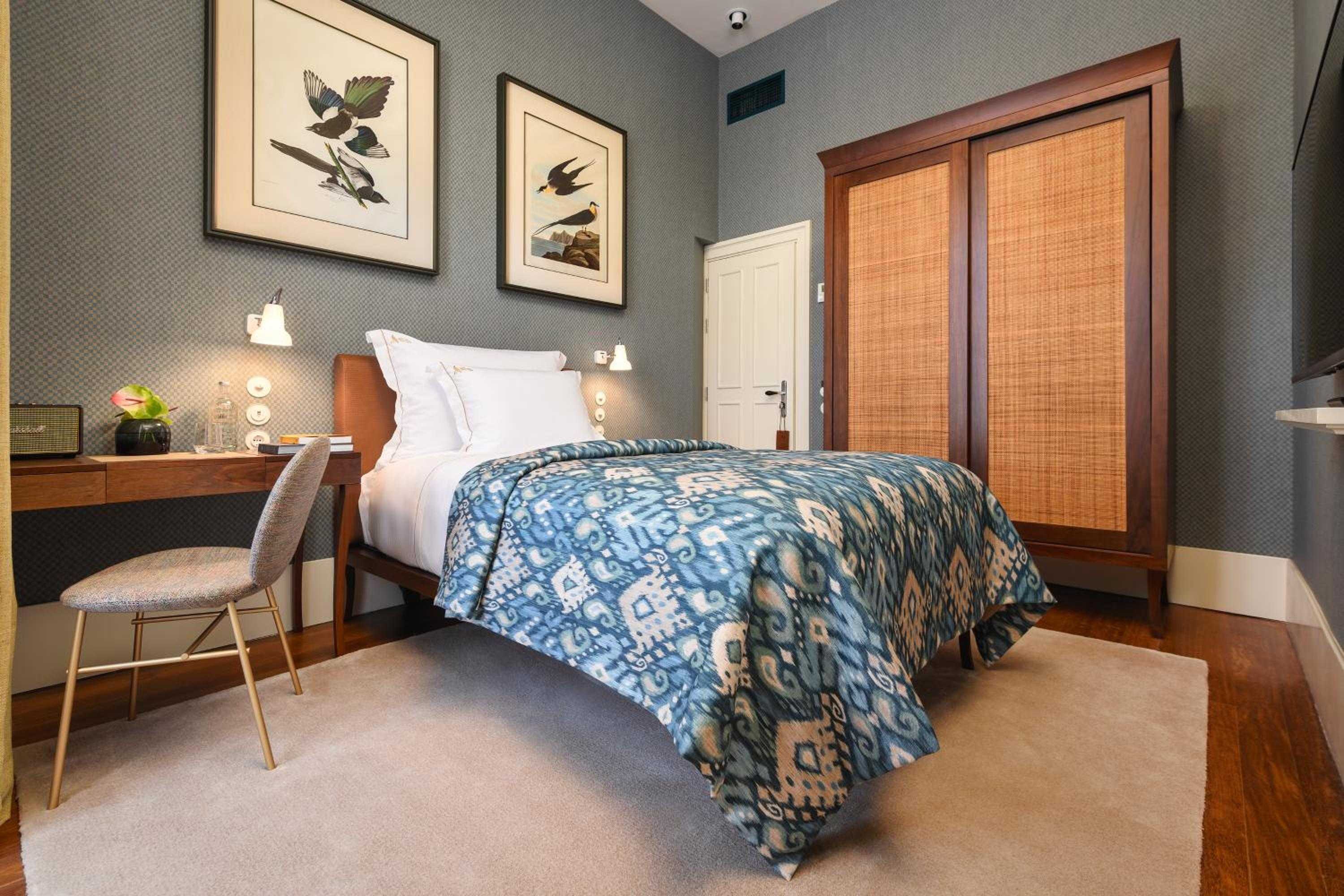 Sophisticated textures define this intimate guest room, where emerald grasscloth wallpaper meets warm wood tones and an ikat-patterned throw drapes casually across crisp linens.