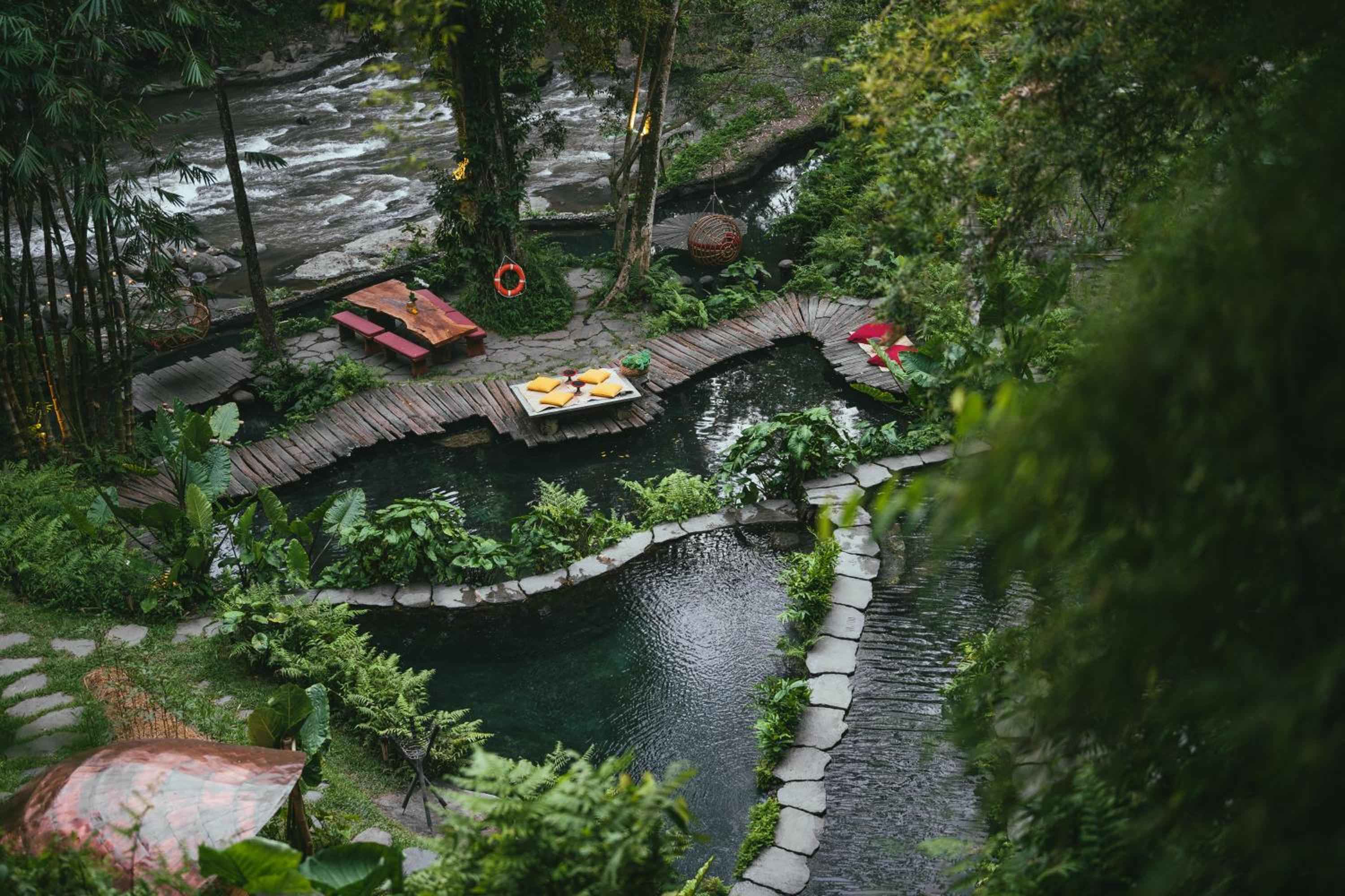 Wooden bridges curve gracefully over crystalline pools, where floating breakfast trays await beneath emerald canopies of tropical palms and ferns.