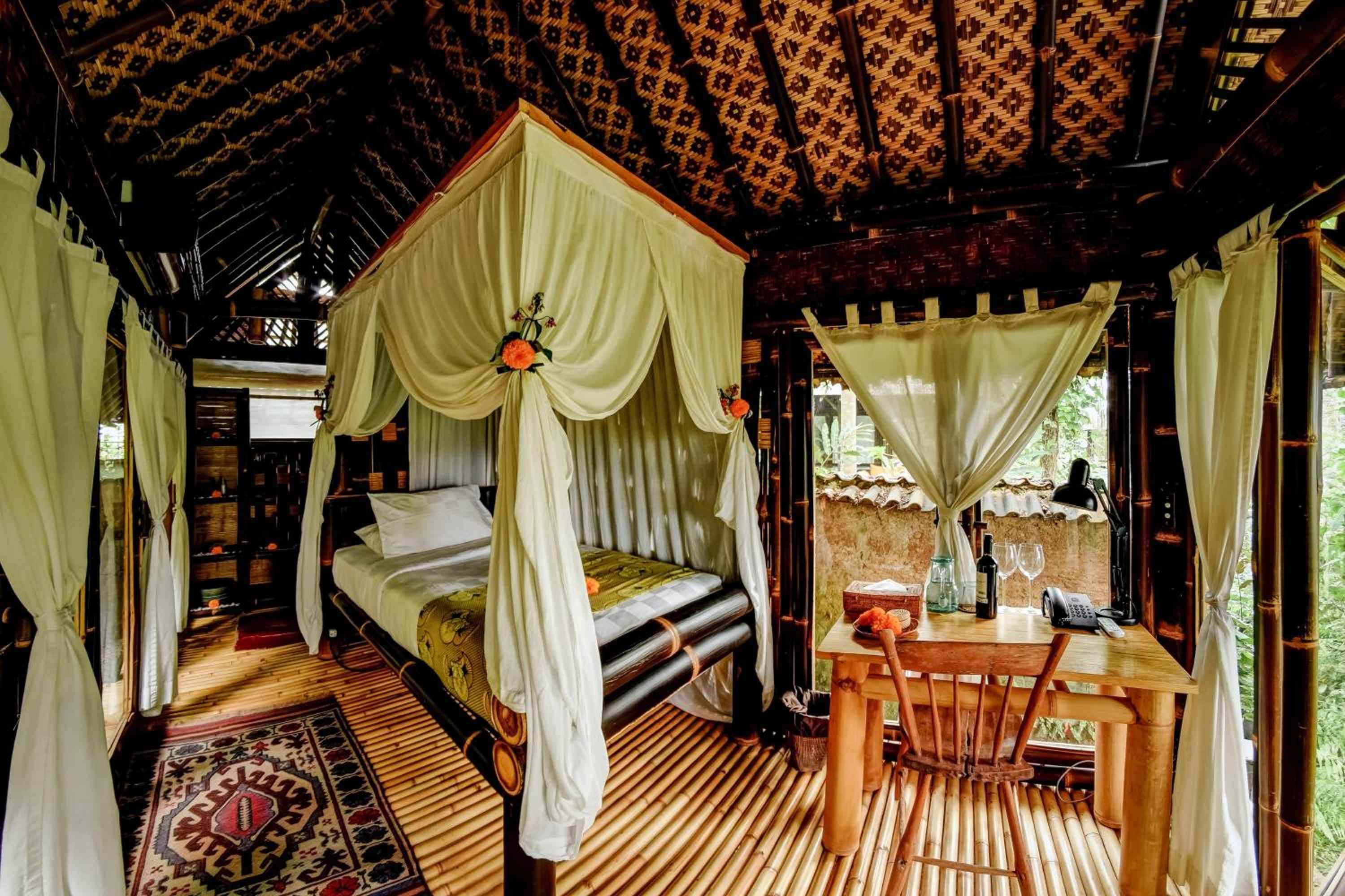 Cream mosquito netting drapes a four-poster bed beneath intricate batik ceiling panels, while bamboo floors and carved furnishings create an intimate Balinese sanctuary.