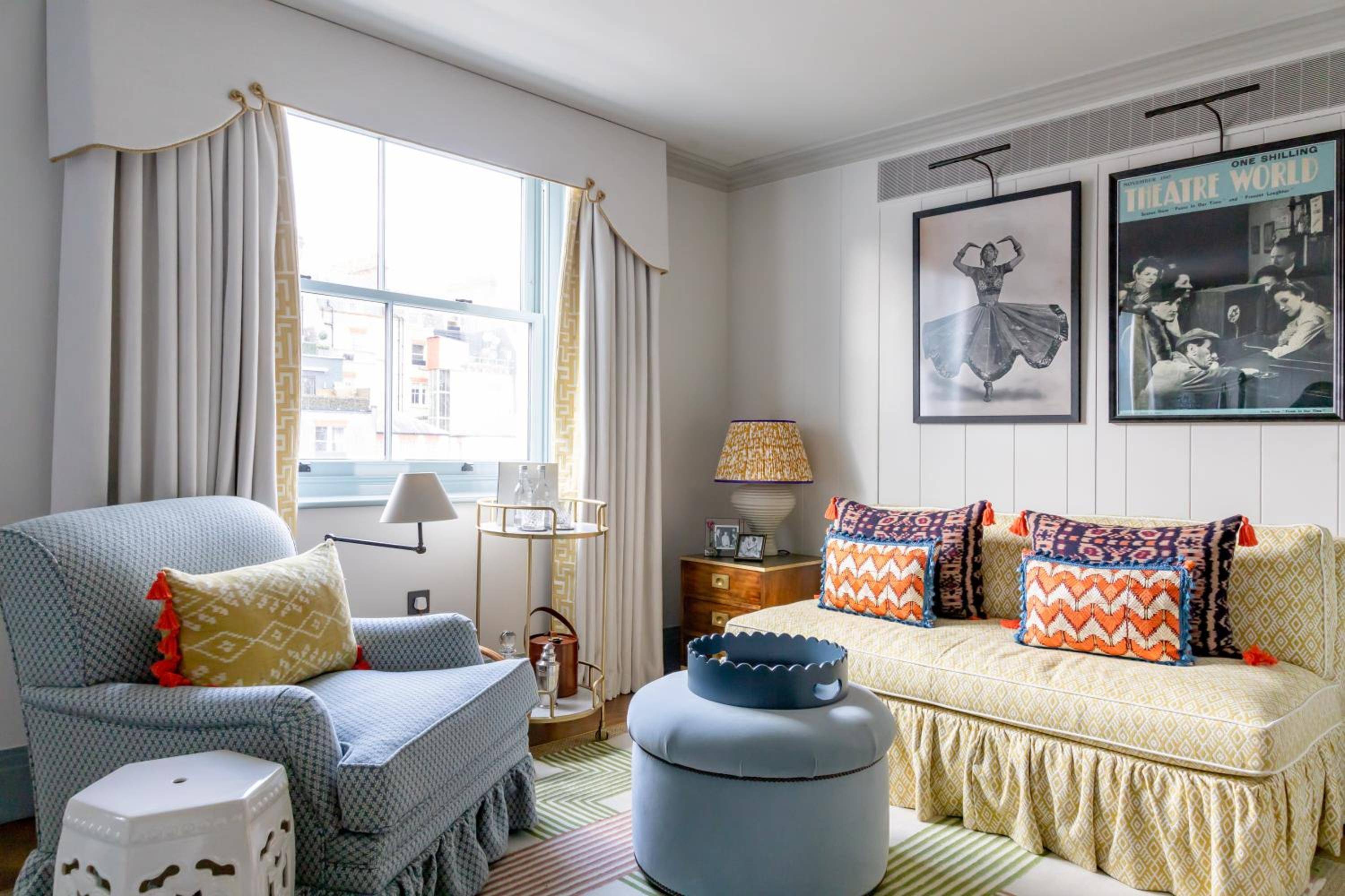 Theatrical posters and jewel-toned cushions create an eclectic sitting room where vintage cinema meets contemporary comfort, natural light streaming across striped rugs and plush fabrics.