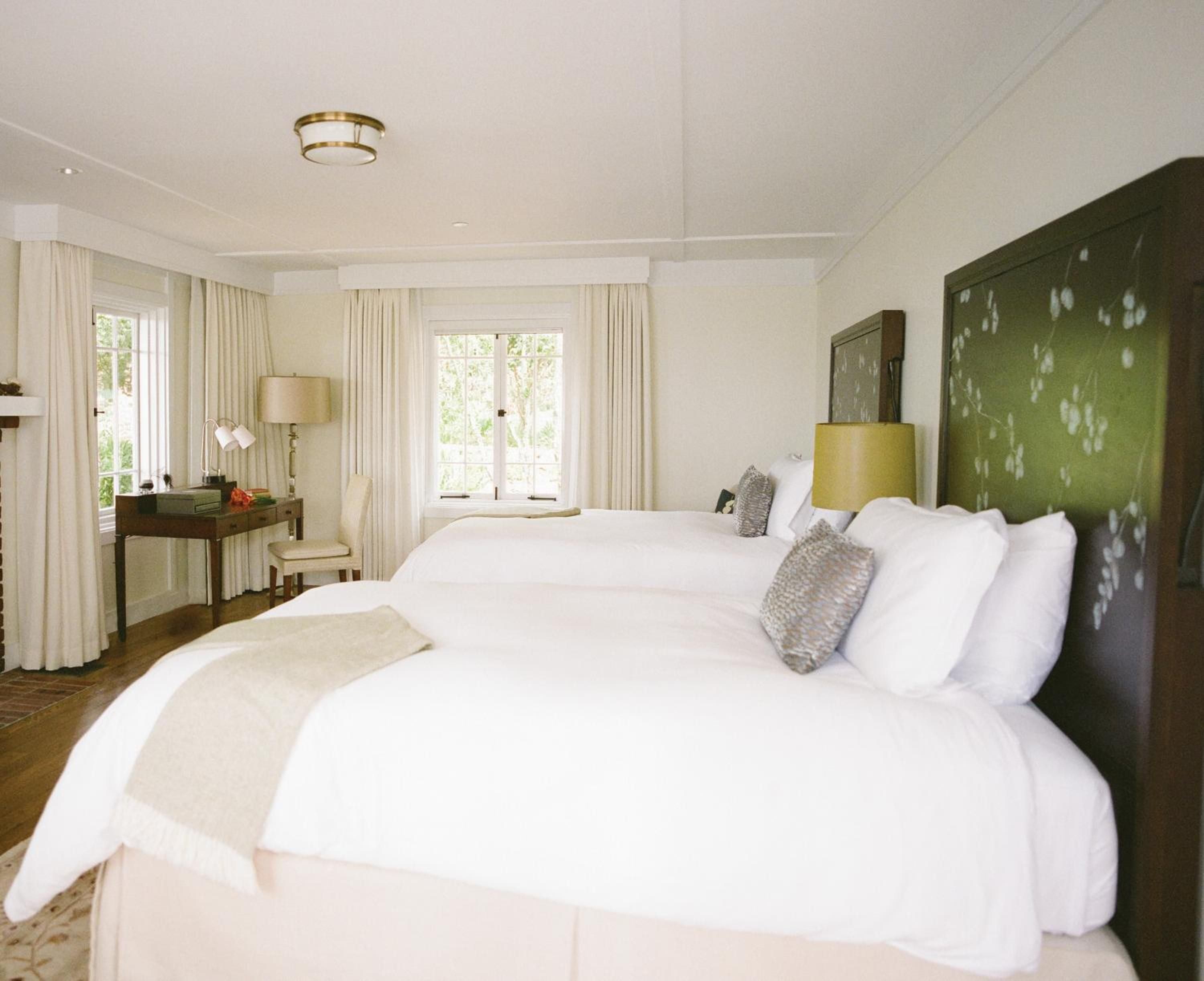Crisp white linens contrast beautifully with the moss-green accent wall, while dappled sunlight filters through sheer curtains in this serene guest room sanctuary.