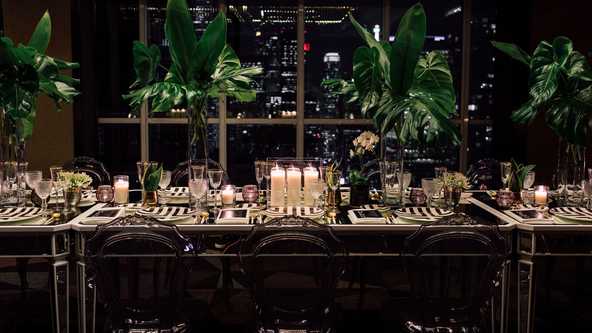 Dramatic tropical centerpieces and flickering candles create an intimate dining atmosphere against Toronto's glittering skyline, where modern elegance meets urban sophistication.