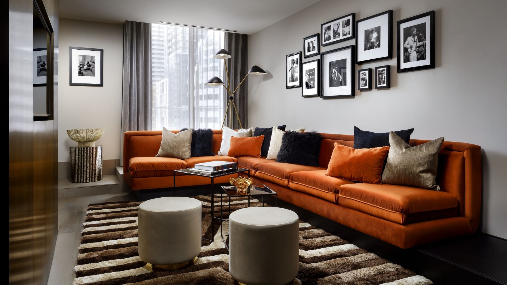 Burnt orange velvet sectionals anchor this sophisticated corner suite, where jazz photography and mid-century lighting create an intimate urban retreat above the cityscape.