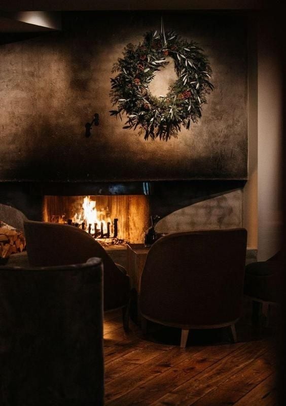 Flickering flames cast golden light across weathered leather chairs beneath a rustic wreath, creating an intimate Nordic sanctuary where guests gather for evening conversations.