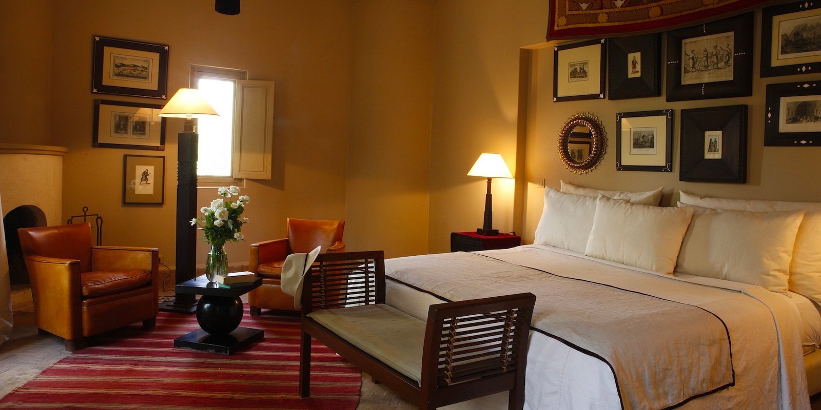 Warm ochre walls embrace this intimate guest room where vintage Moroccan prints create an artful gallery above crisp linens and leather seating bathed in golden lamplight.