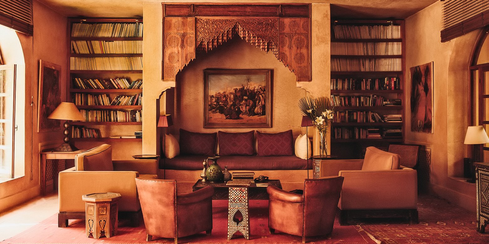 Hand-carved cedar screens frame leather seating in this intimate library corner, where Moroccan craftsmanship meets contemporary comfort beneath warm terracotta walls.