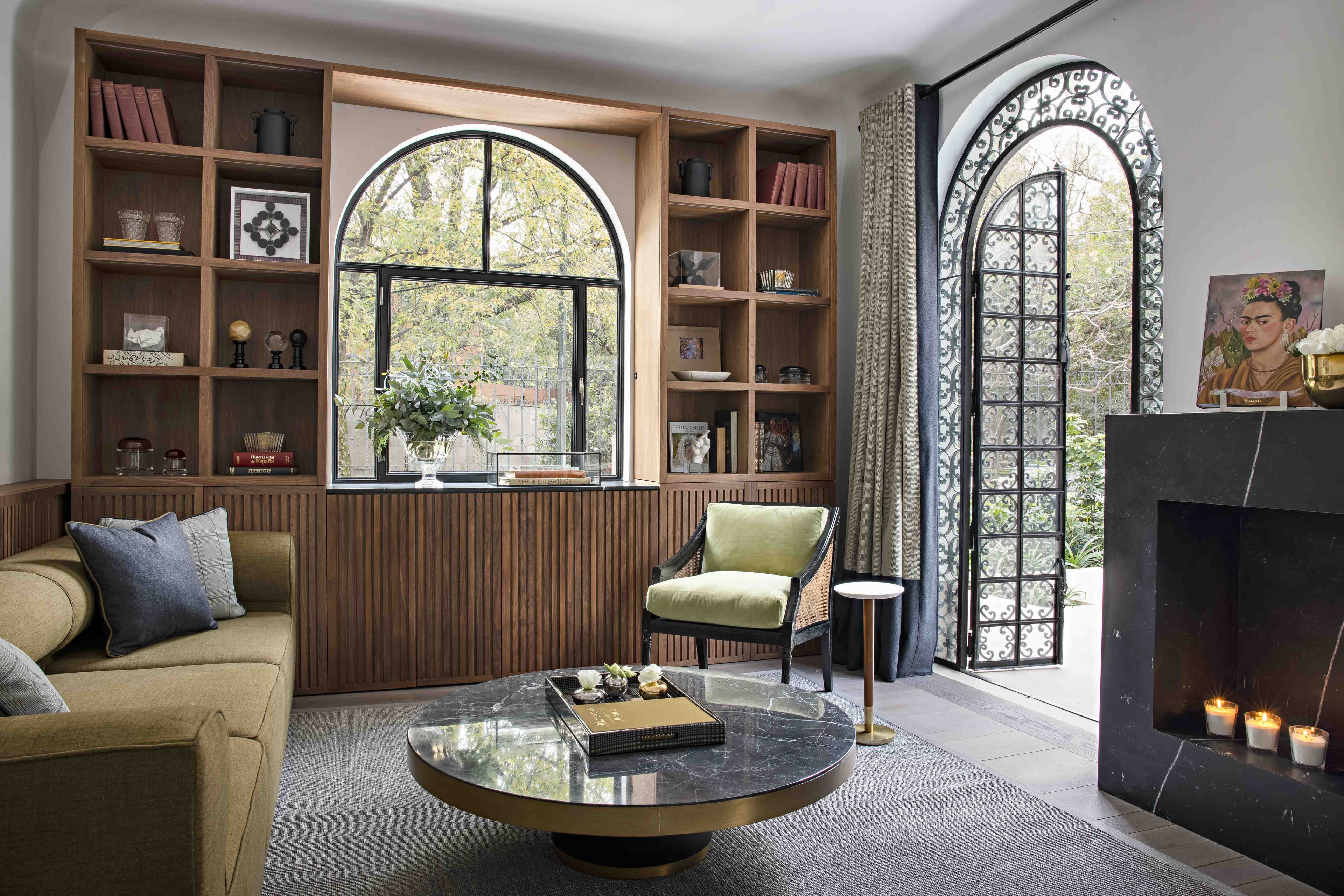 Warm wood built-ins frame an arched window while handwoven textiles and a marble-topped coffee table create an intimate sitting area anchored by flickering candles.