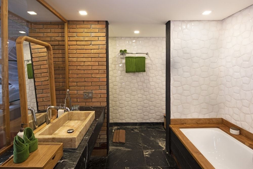 Natural textures harmonize in this serene bathroom retreat where warm brick meets white honeycomb tiles, wooden vanity basins, and deep emerald accents create spa-like tranquility.
