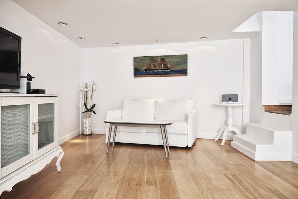 Crisp white walls and honey-toned hardwood floors create a serene sanctuary, where nautical artwork and orchid blooms add subtle character to minimalist elegance.