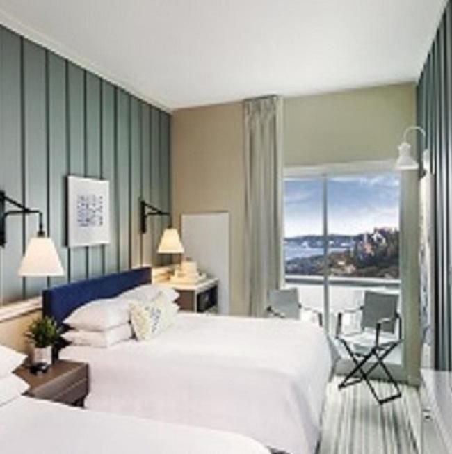 Sage-green board-and-batten walls frame oceanfront views in this sophisticated guest room, where nautical charm meets modern comfort beneath Maine's endless sky.