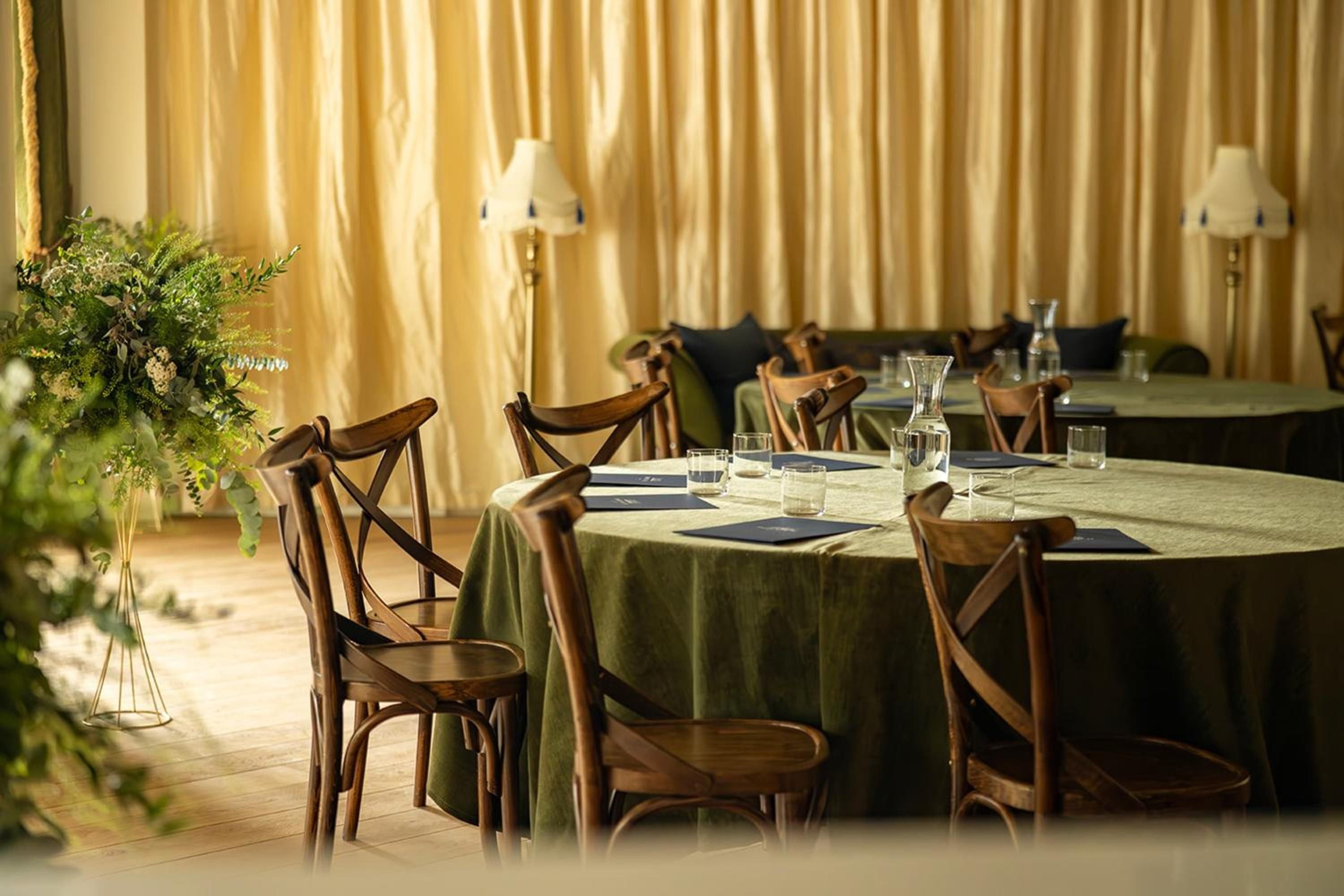 Bentwood chairs gather around sage-colored linens in the intimate dining room, where golden curtains filter Highland light into warm pools across polished floors.