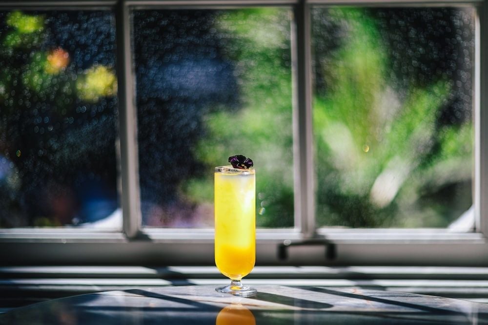 Golden afternoon light streams through rain-kissed windows as a perfectly crafted cocktail awaits, its amber hues echoing the warm, intimate atmosphere of this sophisticated Amsterdam retreat.