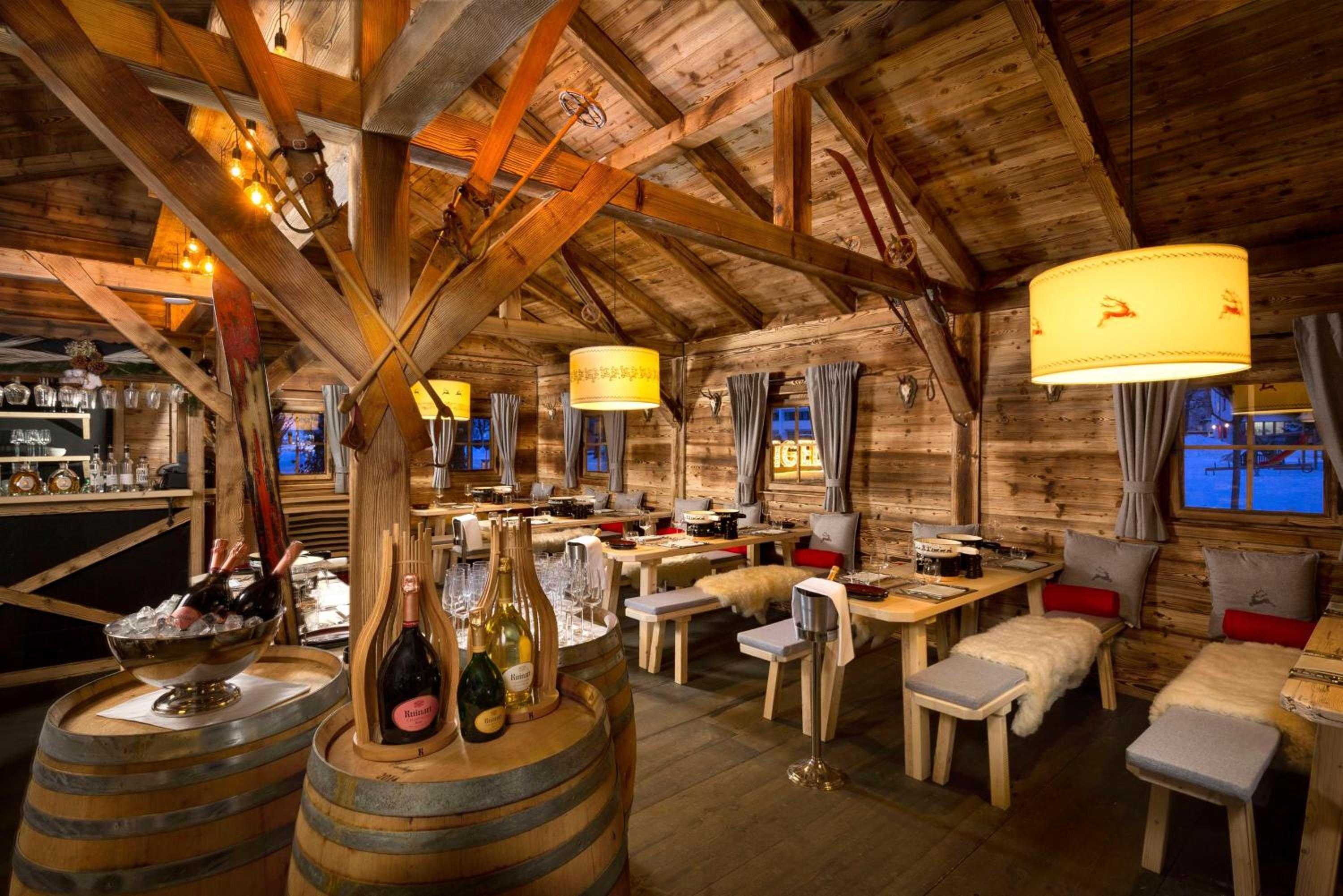 Exposed timber beams and flickering lampshades create intimate alpine charm in this cozy restaurant, where wine barrels double as tables and fur throws invite lingering conversations.