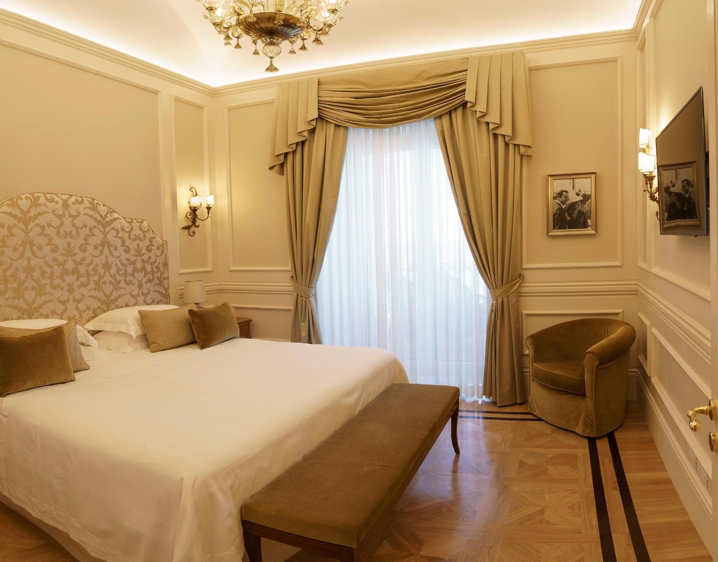 Ornate molding frames this refined guest room where golden silk curtains filter Sorrento sunlight across polished parquet floors and classic damask upholstery.