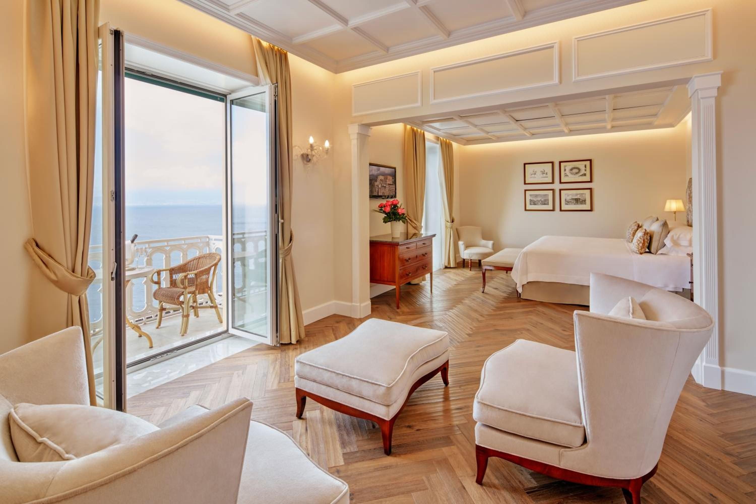 Coffered ceilings and herringbone floors frame this elegant suite, where French doors reveal a private terrace overlooking the sparkling Bay of Naples.
