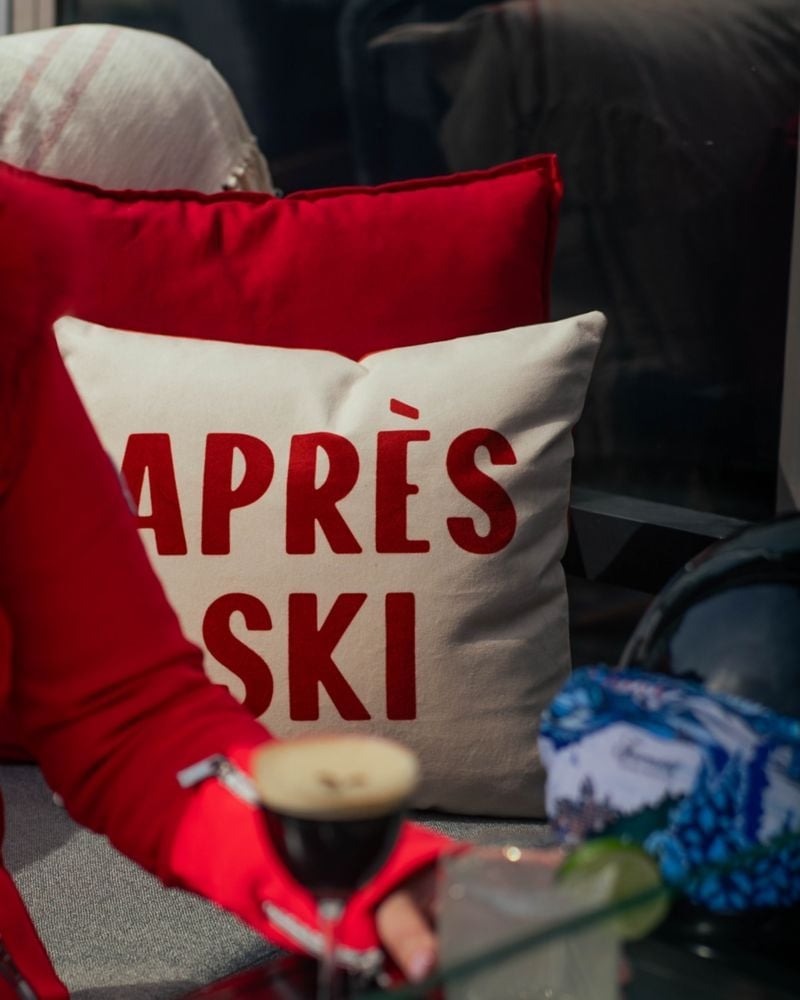 Red pillows emblazoned with 'APRÈS SKI' beckon from plush seating, where steaming mugs and cozy throws promise perfect fireside moments after powder days.
