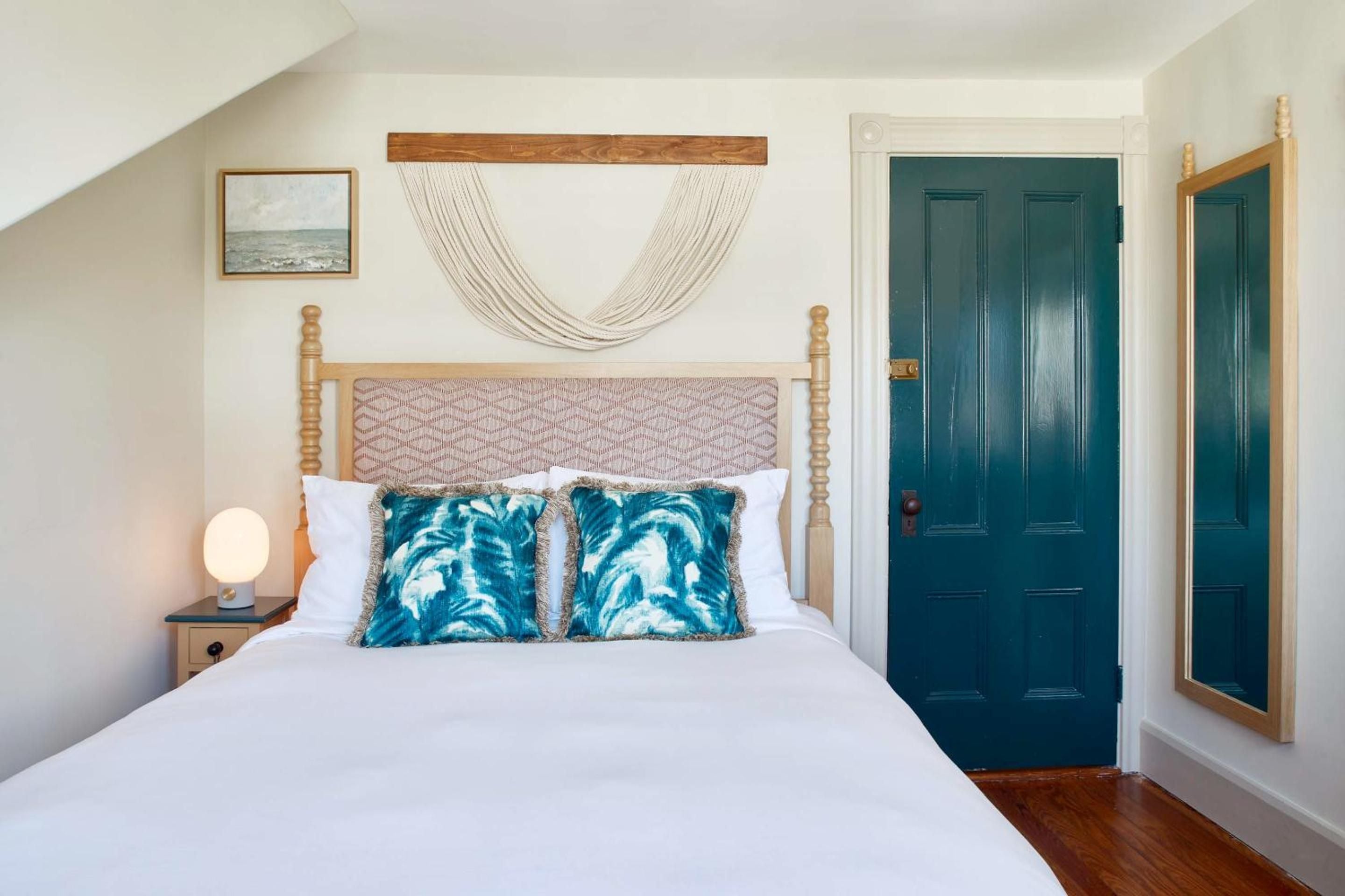 Coastal charm meets cottage comfort in this intimate bedroom, where turquoise pillows echo Nantucket's waters and rope details nod to the island's maritime heritage.
