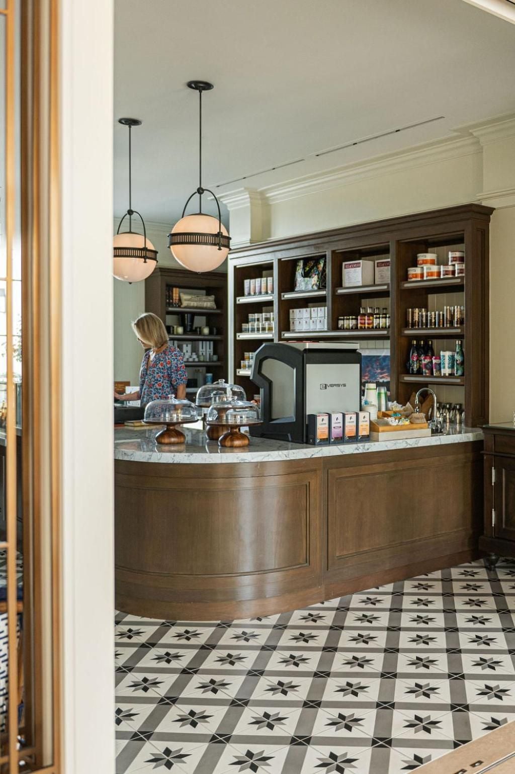 Curved marble countertops and warm wood cabinetry create an inviting coffee bar, where pendant lights cast a golden glow over artisanal treats and geometric tile floors.