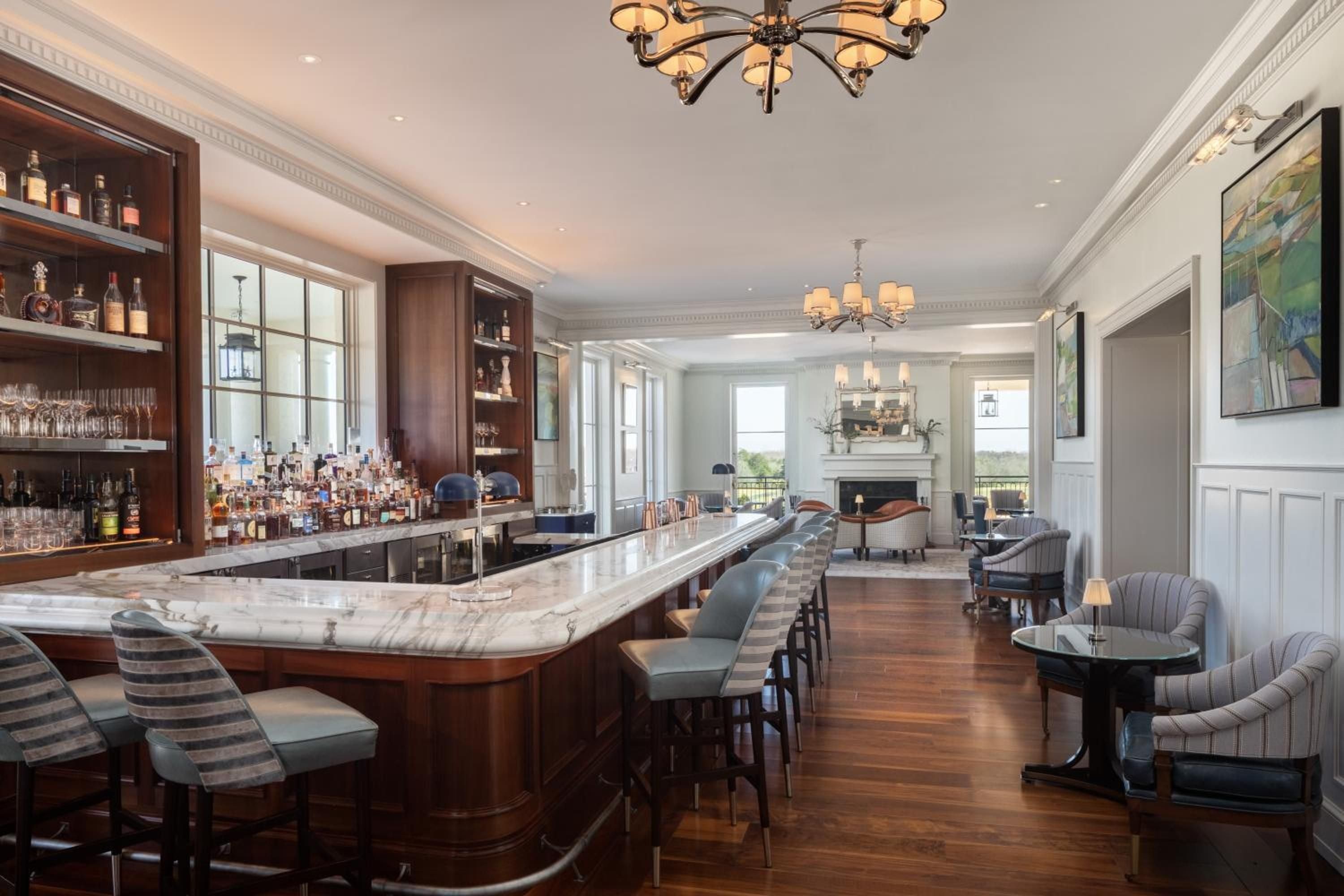 Marble-topped bar gleams under crystal chandeliers while striped banquettes invite intimate conversations in this sophisticated lounge overlooking rolling Virginia countryside.