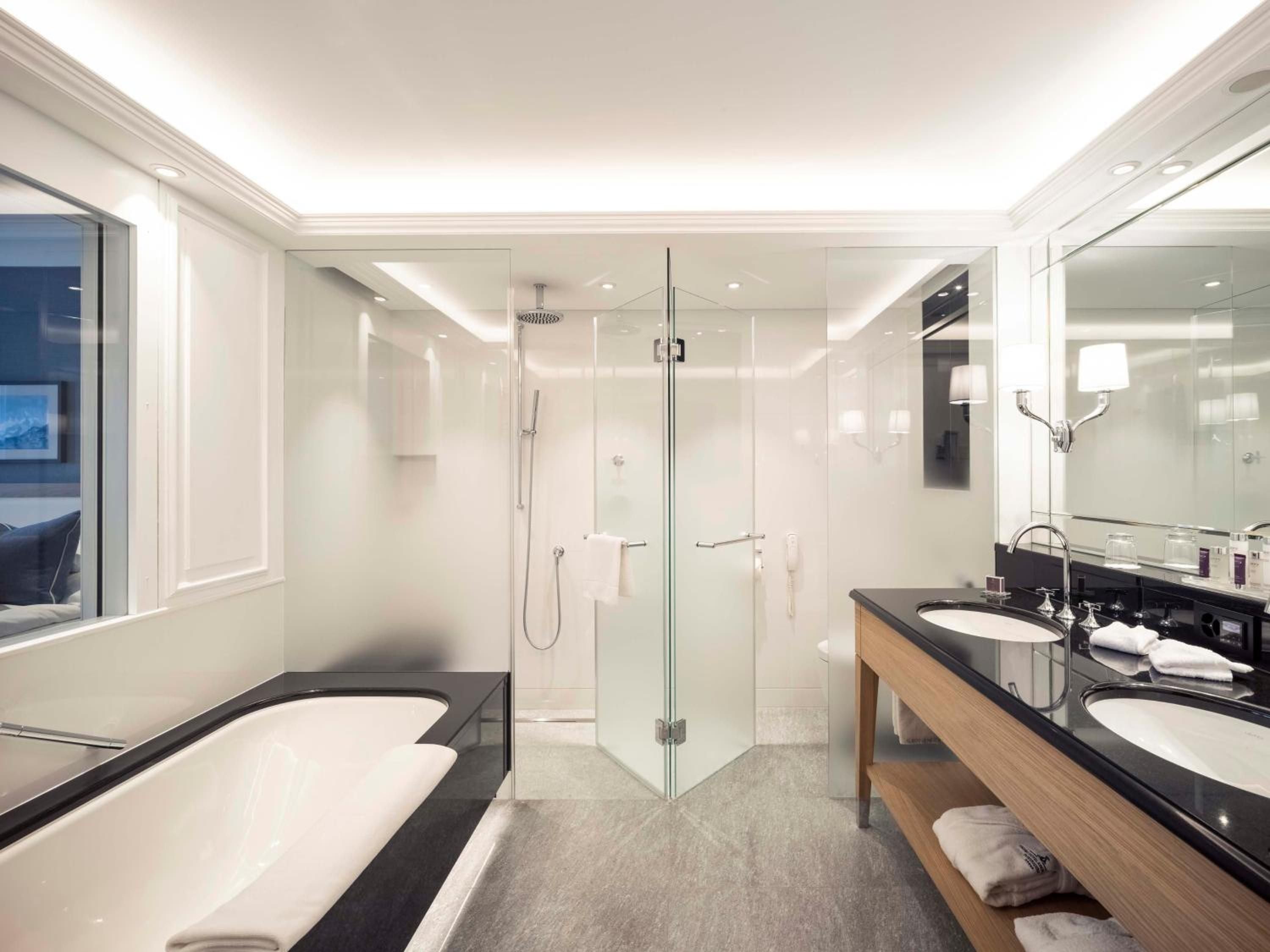 Marble surfaces gleam under soft lighting in this spa-like sanctuary, where deep soaking tubs and rain showers create a serene Alpine wellness retreat.