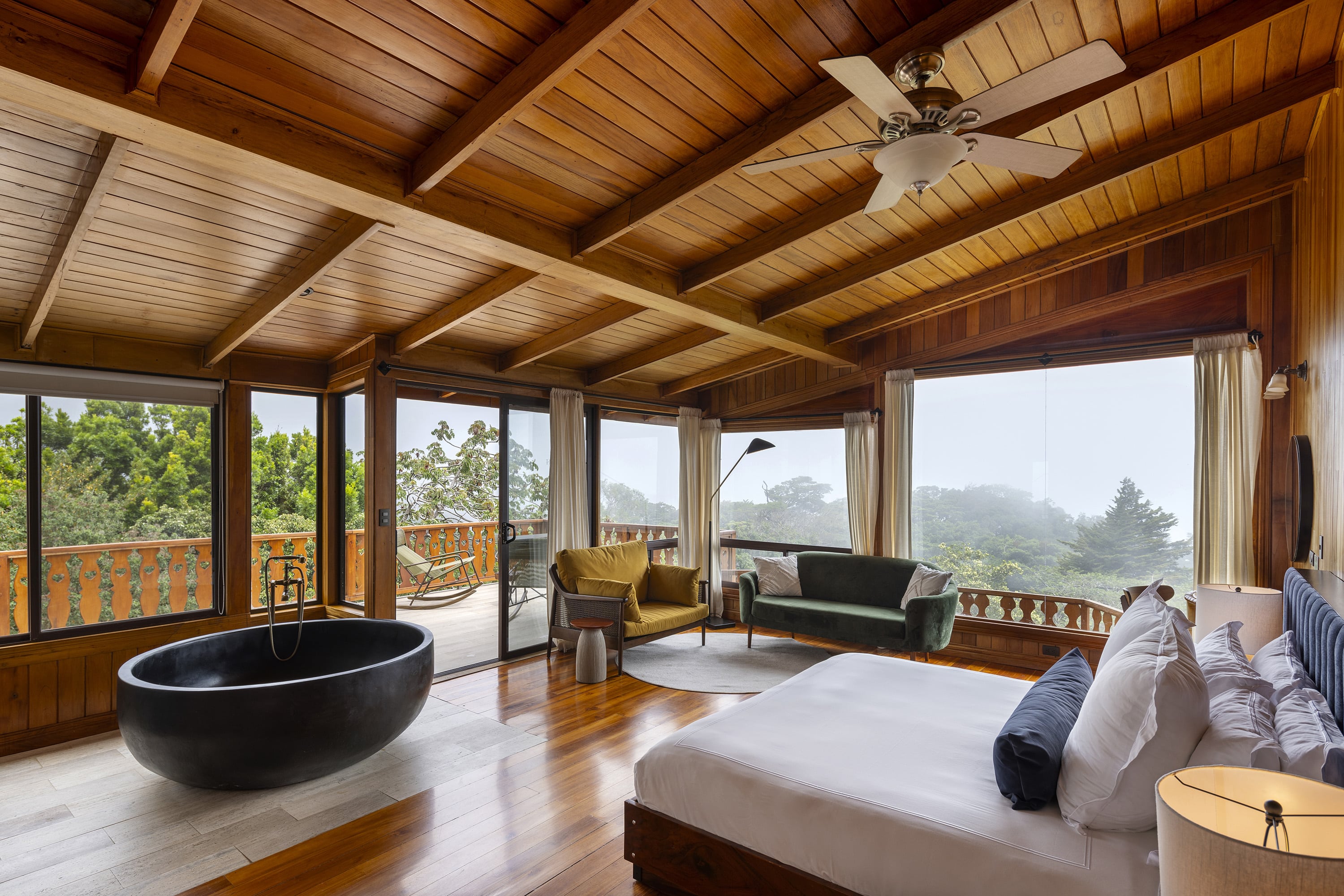 Exposed timber beams frame panoramic forest views in this dreamy suite, where a sculptural black stone bathtub anchors the space beneath soaring cathedral ceilings.