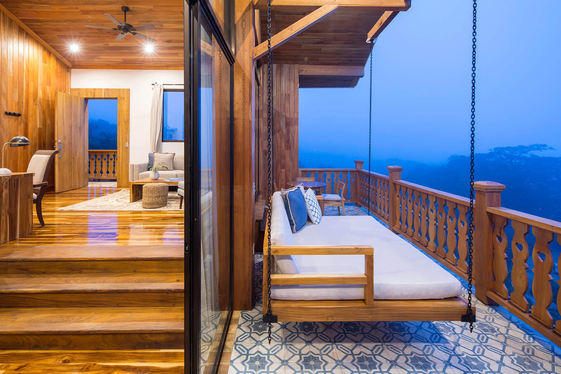 Suspended swing bed chains catch twilight's glow as this open-air suite merges rich teak interiors with panoramic mountain vistas stretching into Costa Rica's misty horizon.