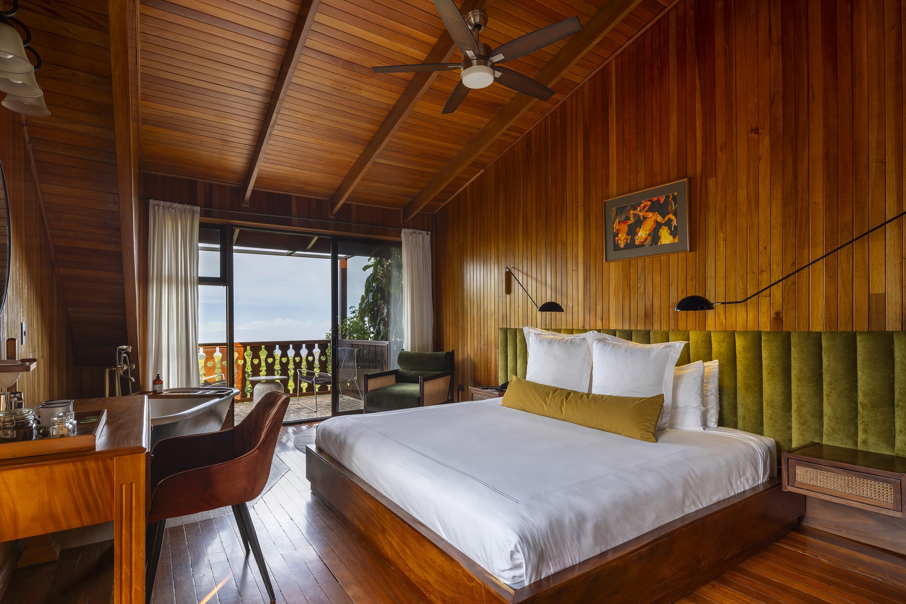Warm teak walls and olive-green velvet headboard create a cozy cocoon, while floor-to-ceiling windows frame verdant mountain views from this thoughtfully appointed sanctuary.