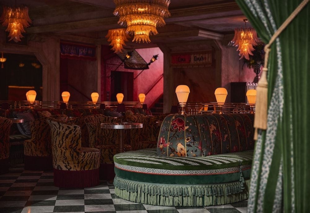 Opulent chandeliers cast amber shadows over plush tiger-print banquettes and emerald velvet, creating an intoxicating speakeasy atmosphere beneath checkered floors.