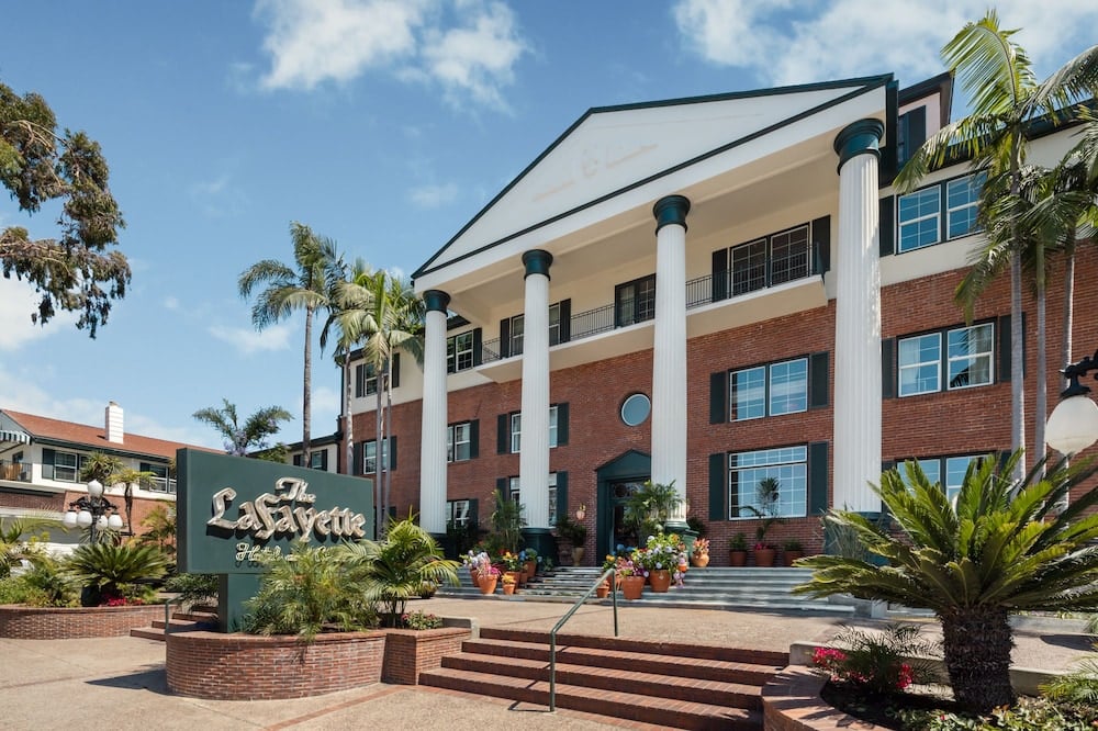 Stately white columns frame the brick facade where tropical palms and terracotta planters create an inviting Southern California welcome beneath crisp blue skies.