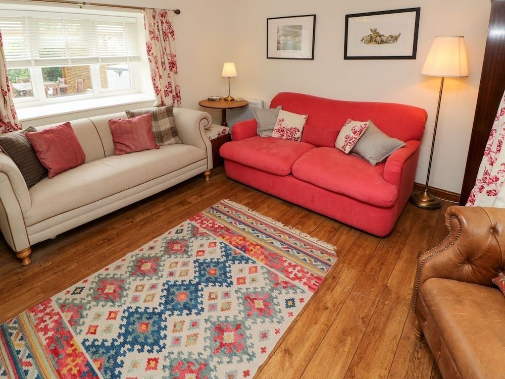 Jewel-toned sofas and a handwoven kilim rug create an inviting sitting room where afternoon light filters through gauzy florals, mixing comfort with countryside charm.