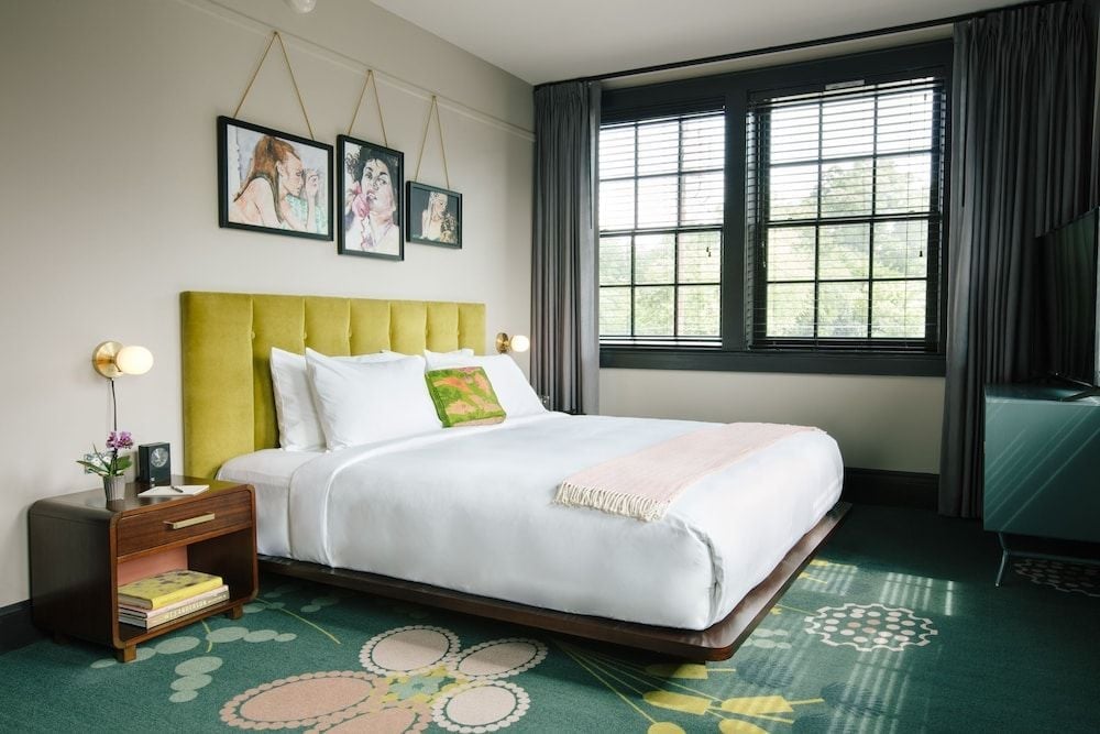 Sunlight streams through black-framed windows onto the whimsical green carpet, where chartreuse velvet meets crisp white linens in this thoughtfully curated guest room.