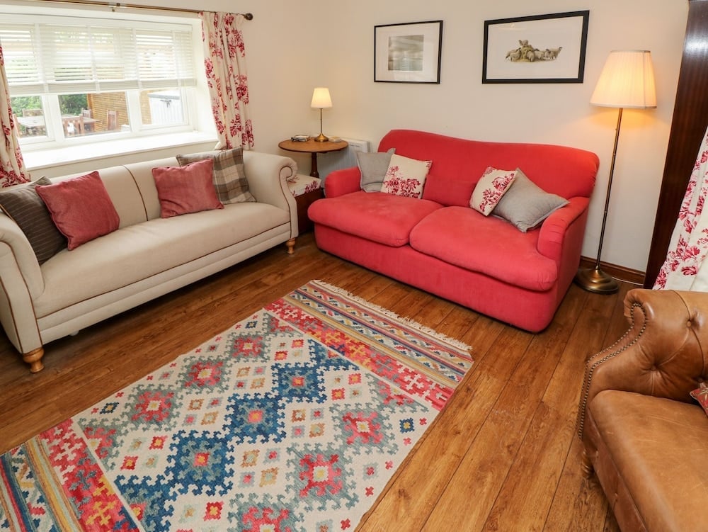 Warm hardwood floors anchor this inviting lounge where coral-red and cream sofas gather around a vibrant geometric kilim, creating an effortlessly stylish retreat.