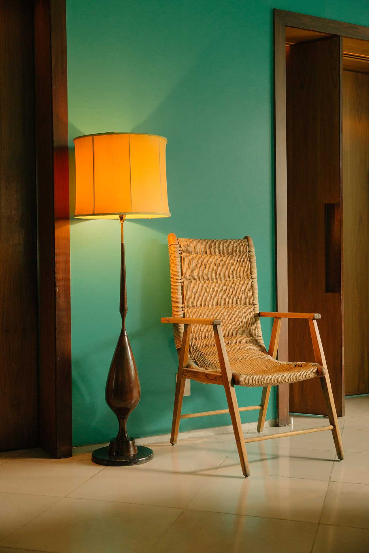 Mid-century charm meets contemporary Mexico City style with a woven rush chair and sculptural brass lamp against turquoise walls that catch golden afternoon light.