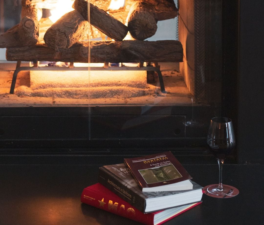 Crackling flames cast amber light across leather-bound books and crystal stemware, creating an intimate reading nook that epitomizes Montreal's sophisticated urban retreat aesthetic.